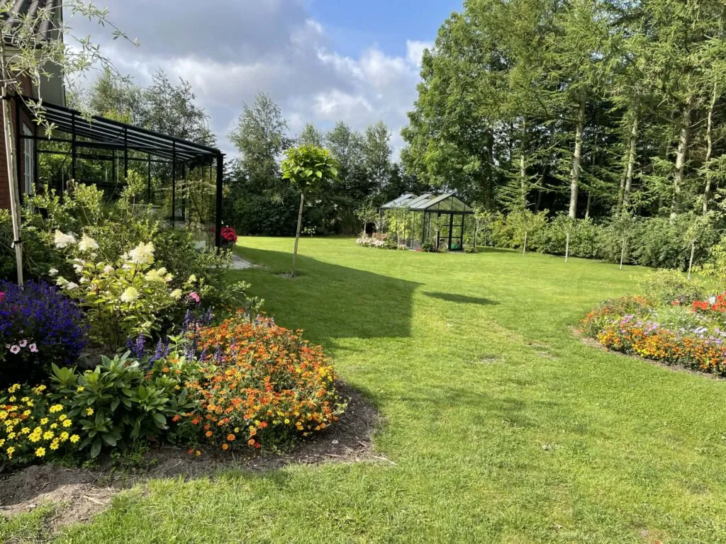 Havestue og drivhus ved den klippede plæne med brogede sommerbede.