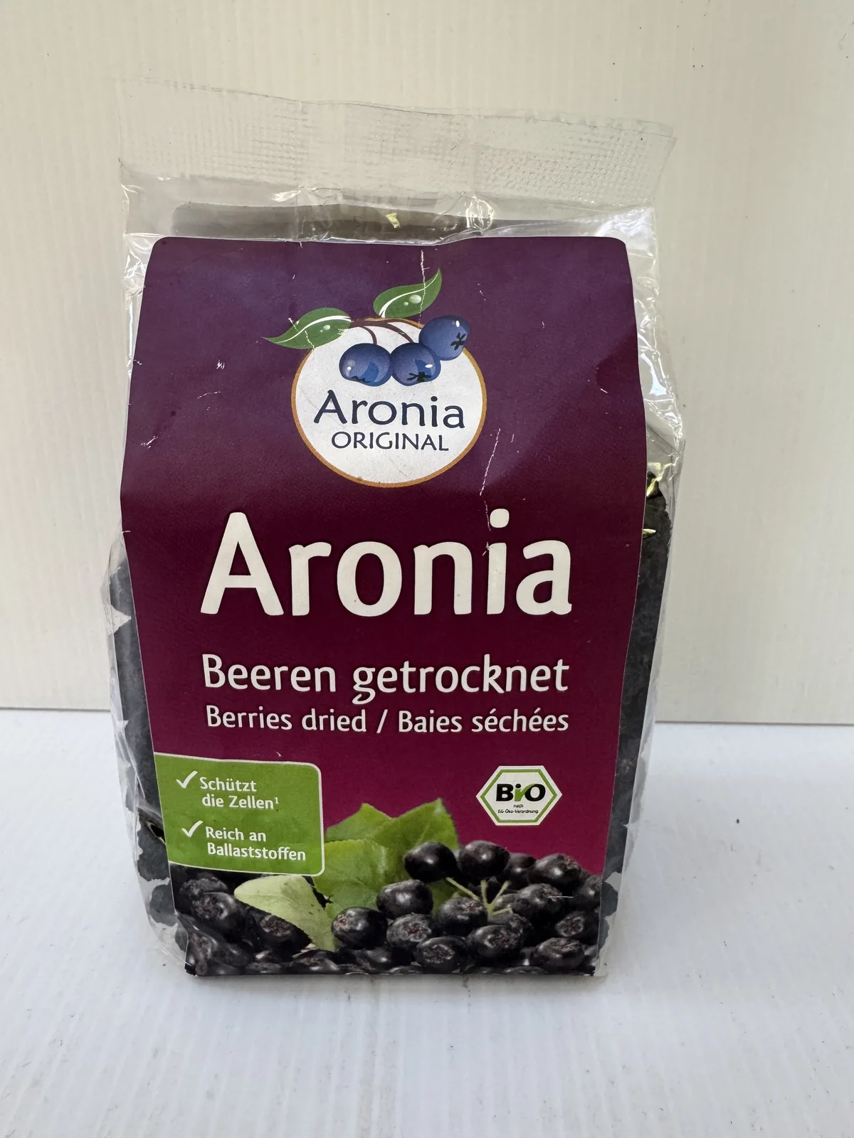 Pose med tørrede aroniabær, et glas yoghurt med bær ovenpå og løse bær foran.