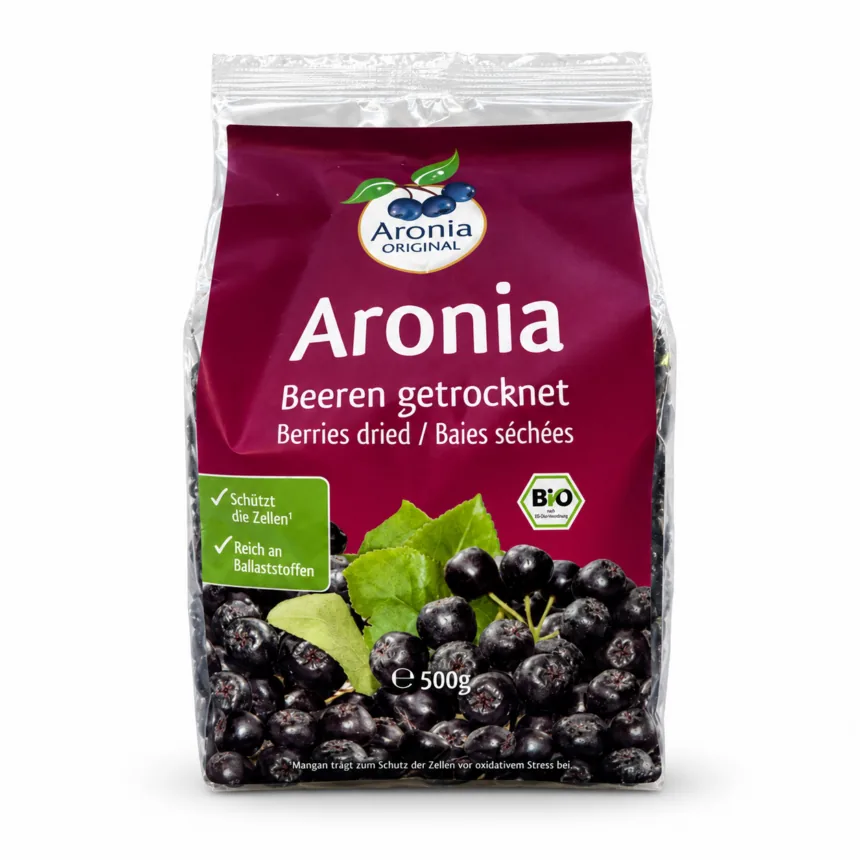 Pose med tørrede aroniabær, et glas yoghurt med bær ovenpå og en håndfuld løse bær foran.