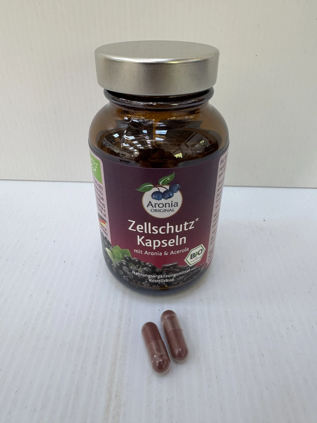 Brun glasflaske med aroniakapsler og to løse kapsler foran.